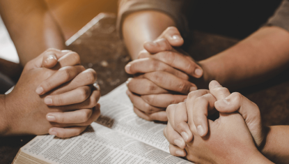 Friends praying over a Bible